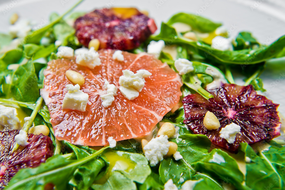 Salad with arugula, grapefruit, red oranges, nuts and cheese. Grey background, top view, close up