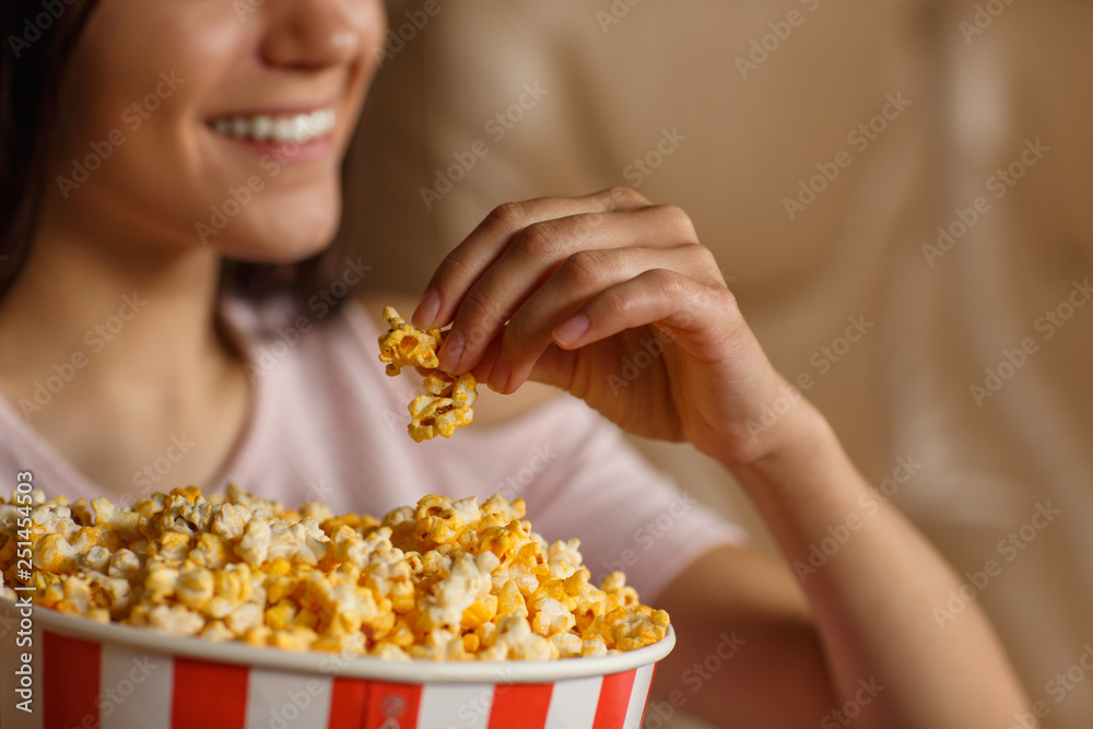 Closeup of delicate female hand keeping cheese popcorn in cinema hall. Young girl laughing and enjoying funny interesting comedy on background. Concept of entertainment and leisure. Closeup of delicate female hand keeping cheese popcorn in cinema hall. Young girl laughing and enjoying funny interesting comedy on background. Concept of entertainment and leisure.