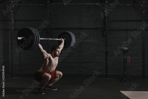 Young crossfit athlete lifting barbell overhead at the gym. Copy space