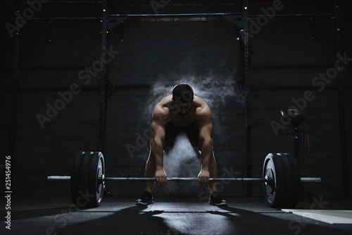 Young crossfit athlete preparing barbell for lifting weight at the gym. Barbell magnesia protection dust cloud. Handsome man doing functional training. Practicing powerlifting. Workout exercises. photo