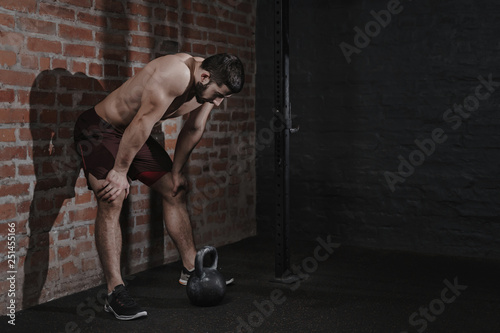 Athlete is leaning against the wall at the gym suffering breakdown to overcome. Demotivation sport concept. Stress and fatigue in sport. Crossfit kettlebell training. Copy space. photo