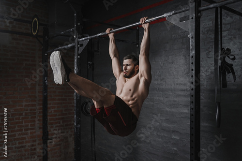 Crossfit athlete doing abs exercises on horizontal bar. Practicing calisthenics at gym.