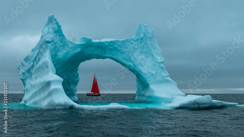 Greenland icerberg arch with red sail ship in Disko bay photo