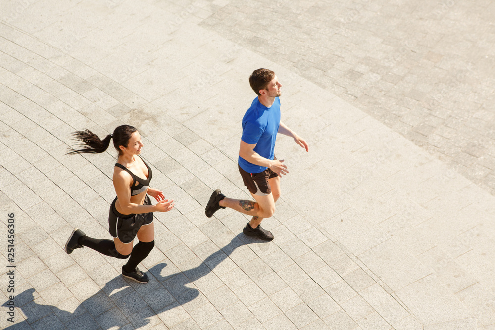 View from above of two young sportsmen wearing tracksuits running together in morning outdoor. Muscular man and fit girl jogging, training and leading healthy lifestyle. Concept of sport.
