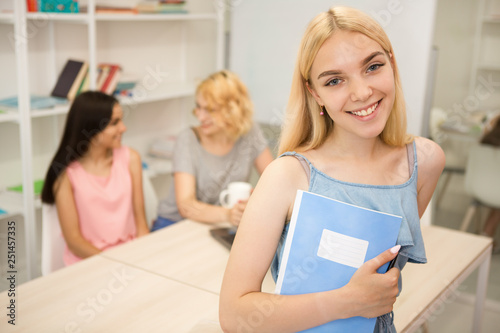 Female student holding notebook and smiling at camera at bright class at college.