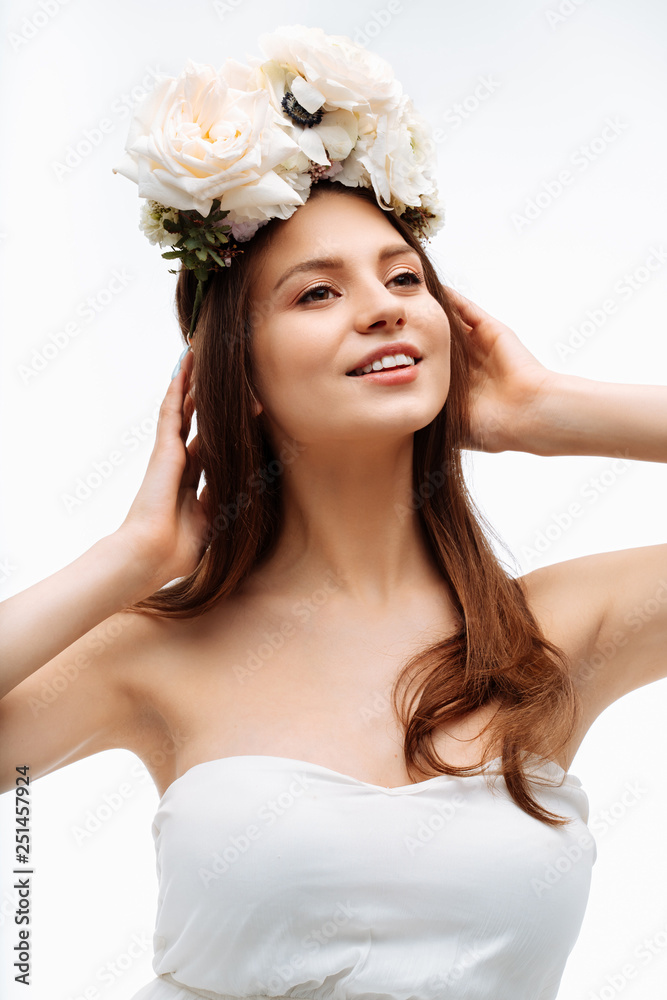 Beautiful young girl smiling and posing with flowers on white background in white dress. Studio portrait. Beautiful young girl smiling and posing with flowers on white background in white dress. Studio portrait.