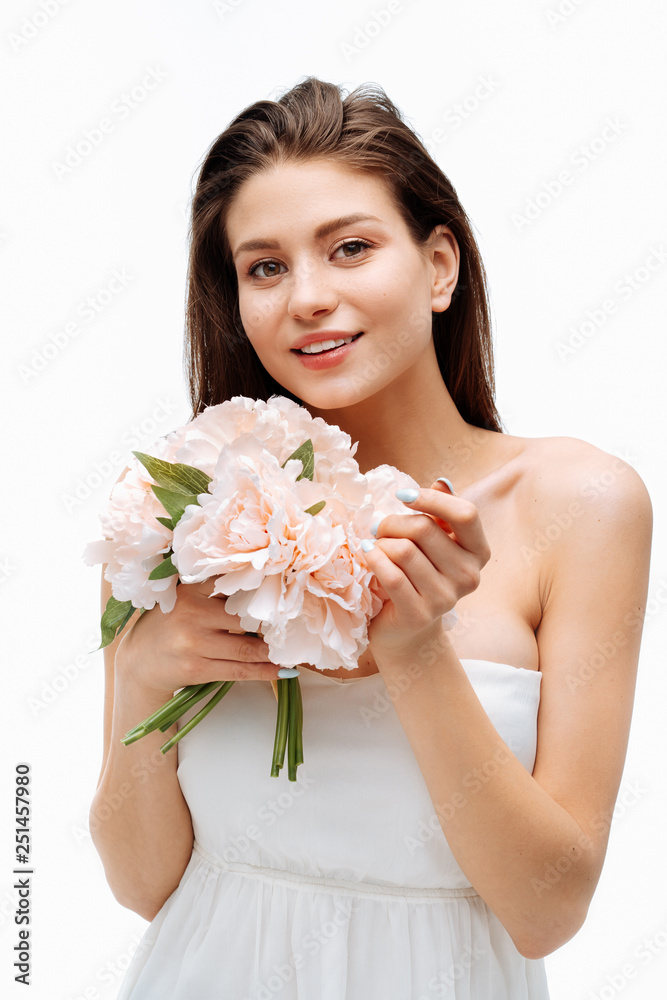 Portrait beautiful young girl smiling and posing with artificial flowers on white background in white dress. Portrait beautiful young girl smiling and posing with artificial flowers on white background in white dress.