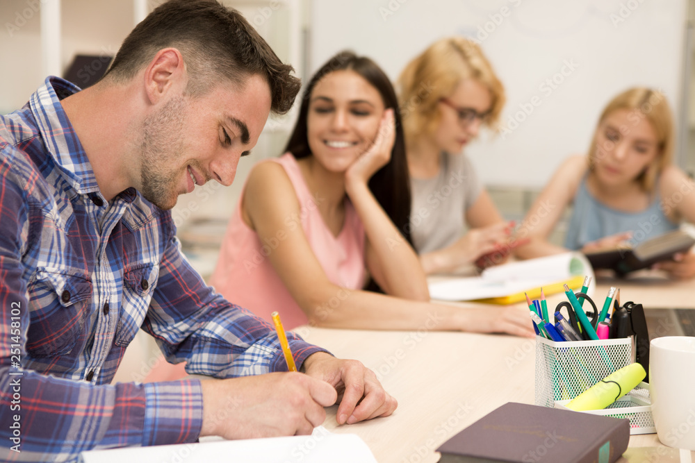 Side view of handsome man sitting at table and writing lecture in notebook. Side view of handsome man sitting at table and writing lecture in notebook.