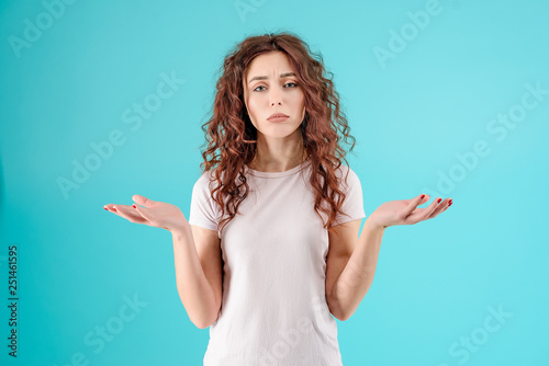 Attractive brunette girl with curly hair isolated over blue turquoise background with unhappy and sad face. Hangover concept