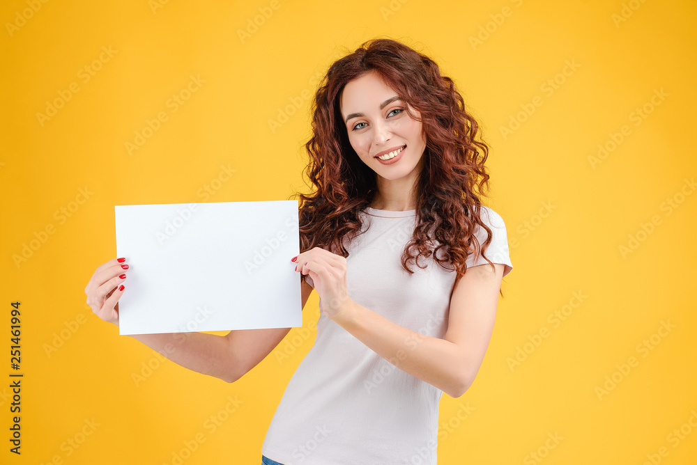 Attractive brunette girl with curly hair isolated over yellow background with a copyspace white paper in her hands Attractive brunette girl with curly hair isolated over yellow background with a copyspace white paper in her hands
