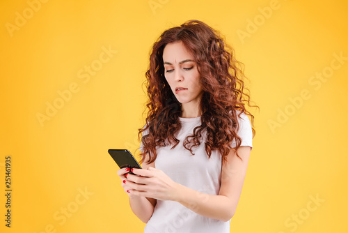 Attractive brunette girl with curly hair isolated over yellow background using mobile app for communication