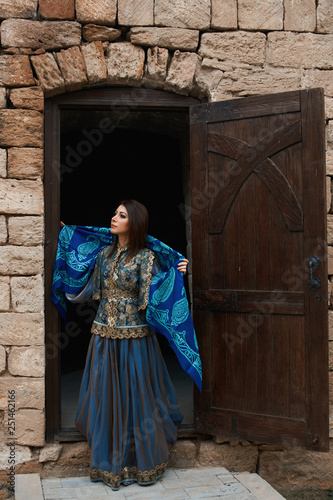 Beautiful girl in traditional dress comes out of the door of a brick house