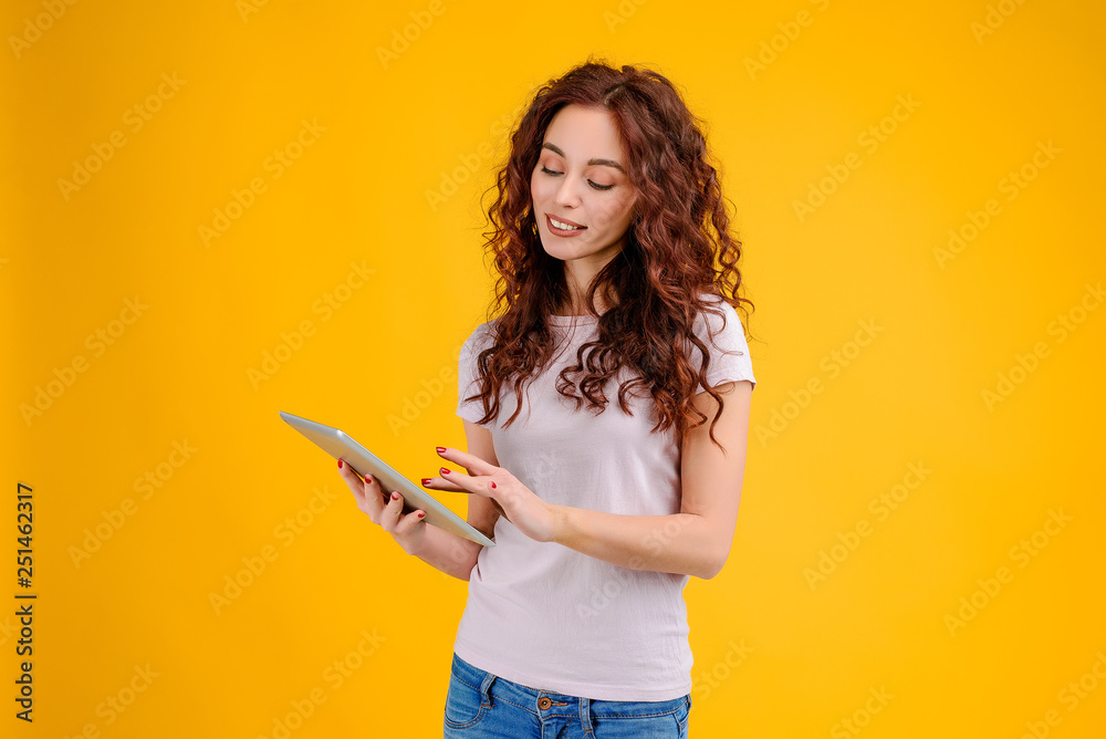 Attractive brunette girl with curly hair isolated over yellow background smiling shopping online and using a new app from tablet. Business concept Attractive brunette girl with curly hair isolated over yellow background smiling shopping online and using a new app from tablet. Business concept