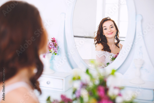 Beautiful young bride looks in the mirror and smiles