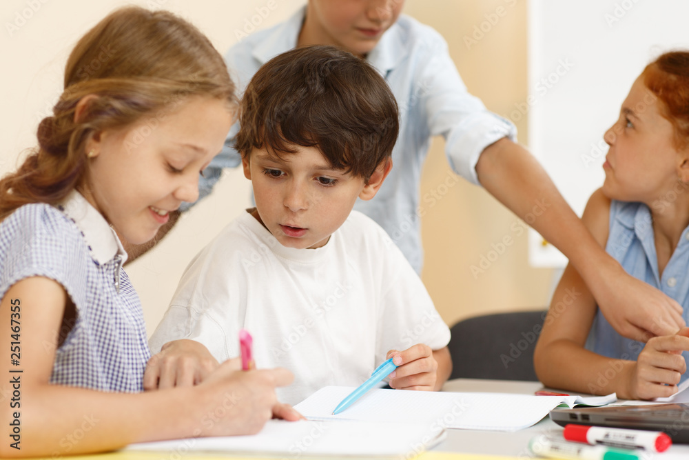 Curious little student of modern school sitting near girl in looking her copybook and asking her in classroom. Schoolboy talking with classmate while learning new material an school. Curious little student of modern school sitting near girl in looking her copybook and asking her in classroom. Schoolboy talking with classmate while learning new material an school.