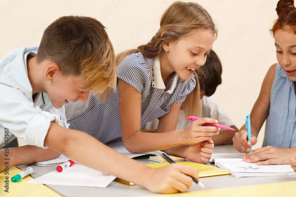 Interested schoolgirl working in team with classmates during lesson in school. Cute student talking with friends, writing in copybook and doing tasks in classroom. Concept of modern education. Interested schoolgirl working in team with classmates during lesson in school. Cute student talking with friends, writing in copybook and doing tasks in classroom. Concept of modern education.
