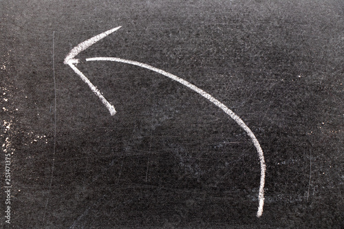 White chalk hand drawing in moving left arrow shape on black board background