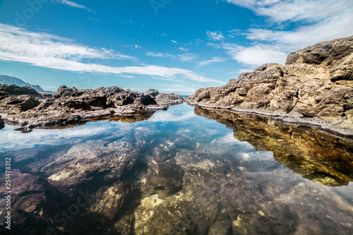 Queen`s Bath on Kauai, Hawaii island. Ocean pond in rocks with sky reflection.