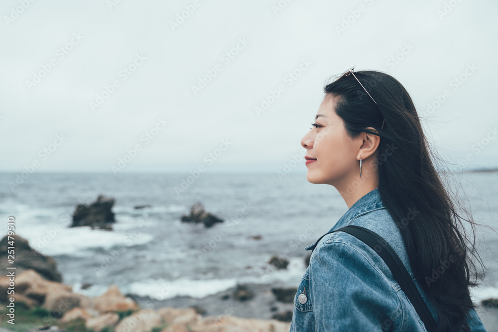 side view happy girl tourist standing on cliff overlooking ocean with her hair blowing. young female chinese backpacker relaxing in nature sea wild lifestyle. girl student trip monterey peninsula