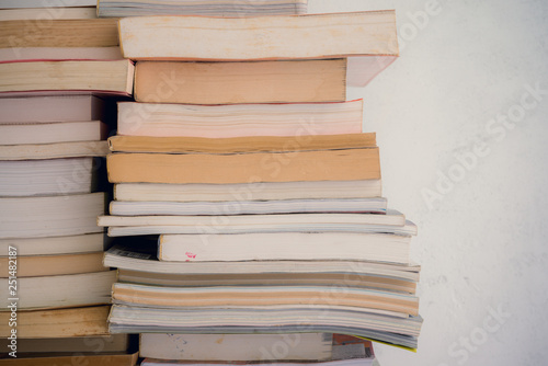 Stack of many old books on shelf in book store or library room with white wall background, vintage tone. Knowledge learning, education, bachelor degree in university or back to school concept.