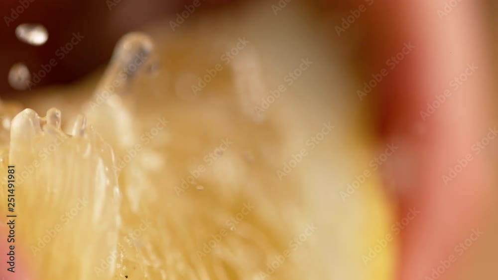 MACRO, DOF, SLOW MOTION: Quarter of organic lemon is squeezed and sour juice squirts out. Fresh lemon juice explodes out of a lemon slice being squeezed. Aromatic droplets of liquid splashing wildly.