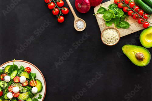 Ingredients for fresh salad. Vegetables, greens, spices, plate of salad on black background top view space for text