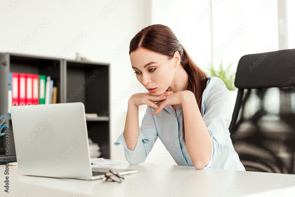 Business concept - successful young and concentrated business woman sitting at her desk working at the laptop in the office Business concept - successful young and concentrated business woman sitting at her desk working at the laptop in the office