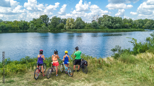 Family on bikes cycling outdoors, active parents and kids on bicycles, aerial view of happy family with children relaxing near beautiful river from above, sport and fitness concept