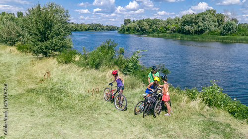 Family on bikes cycling outdoors, active parents and kids on bicycles, aerial view of happy family with children relaxing near beautiful river from above, sport and fitness concept