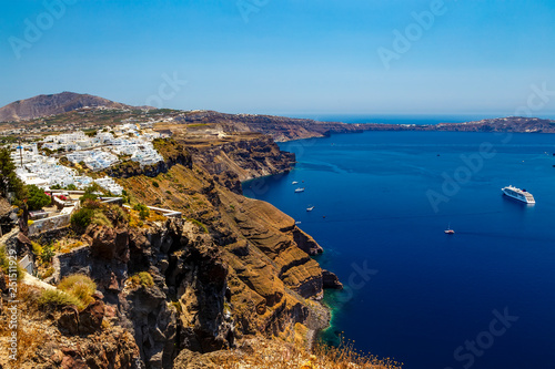 View of Santorini volcanic landscape, sea with a sailing ship, motor boats
