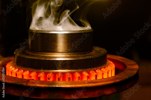 closeup calcining hot metal steel gear parts in a factory induction furnace with smoke