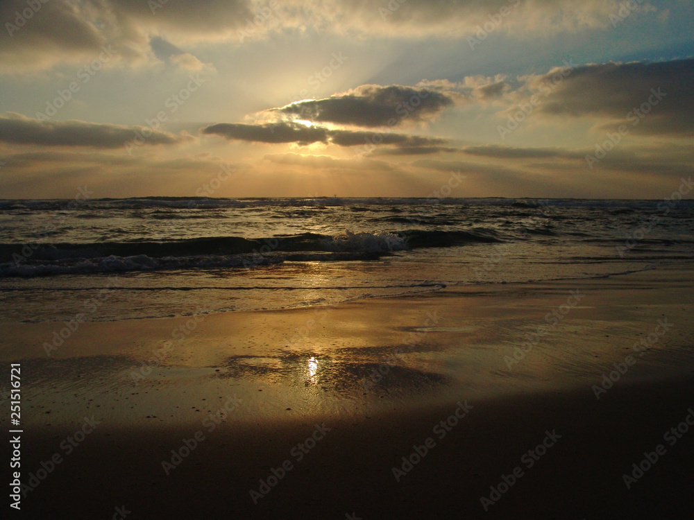 Sunset view on a calm sandy beach with cloudy sky and golden light.