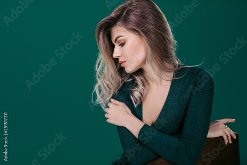 Sensual beautiful blonde woman in green dress sitting on chair against green background © producer