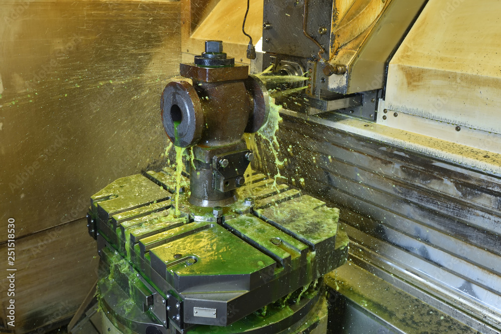 The process of drilling and grinding holes in the body of the valve on the CNC machine. Yellow-green coolant splashes into place The process of drilling and grinding holes in the body of the valve on the CNC machine. Yellow-green coolant splashes into place