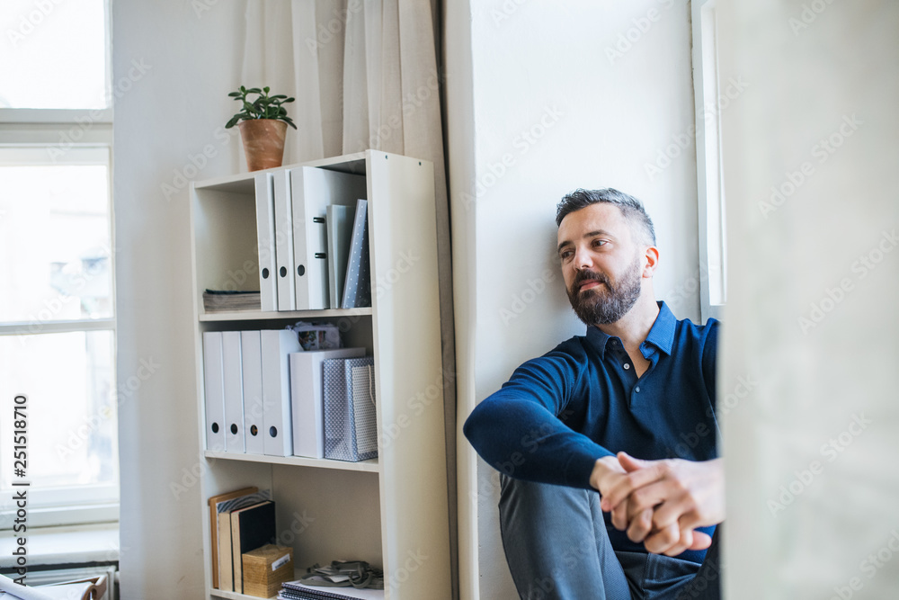 Mature hipster businessman sitting on a window sill in a modern office.