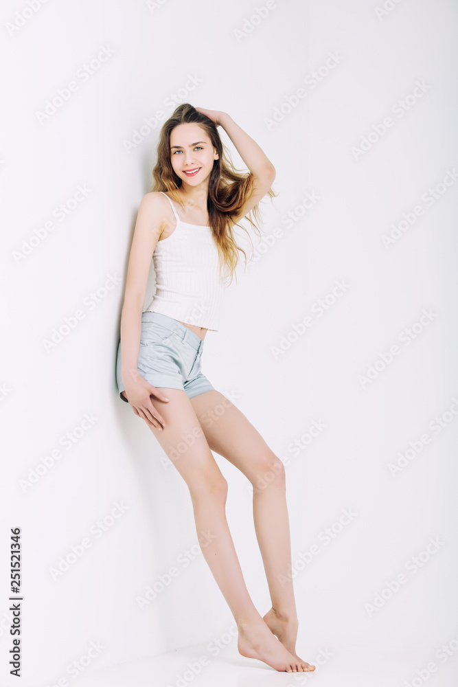 Model beautiful young girl with blond hair and blue eyes in a t-shirt and shorts fashionable in the Studio