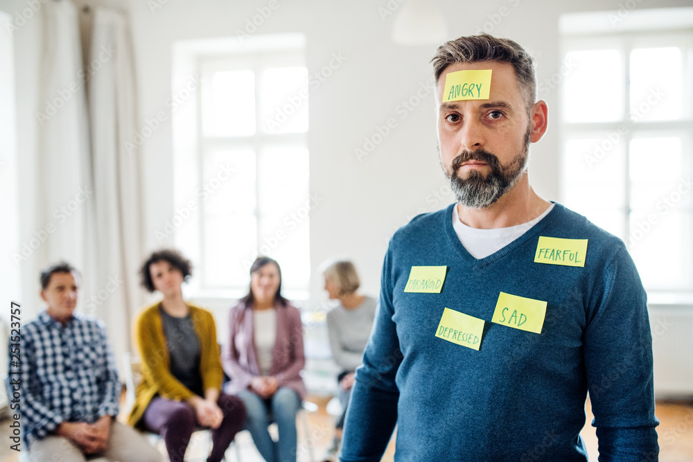 Fototapeta premium Mature man standing with negative emotions adhesive notes during group therapy.