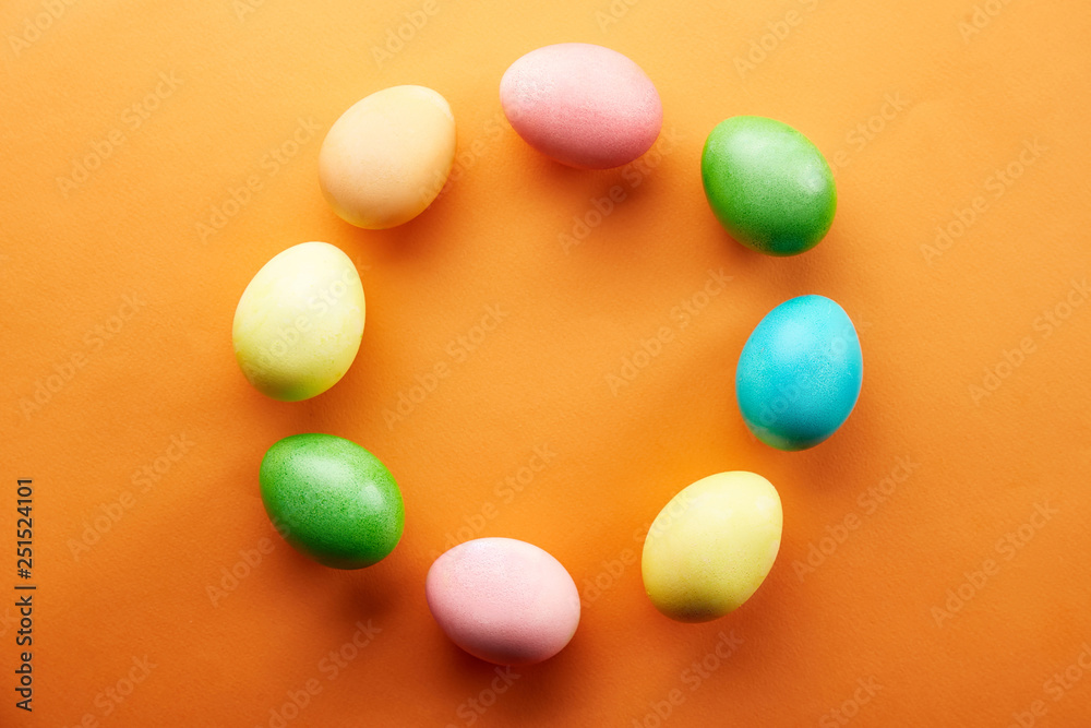 Bunch of blank painted Easter eggs of different pastel color on bright orange paper background with a lot of copy space for text. Top view, flat lay, close up. Easter greeting card concept.