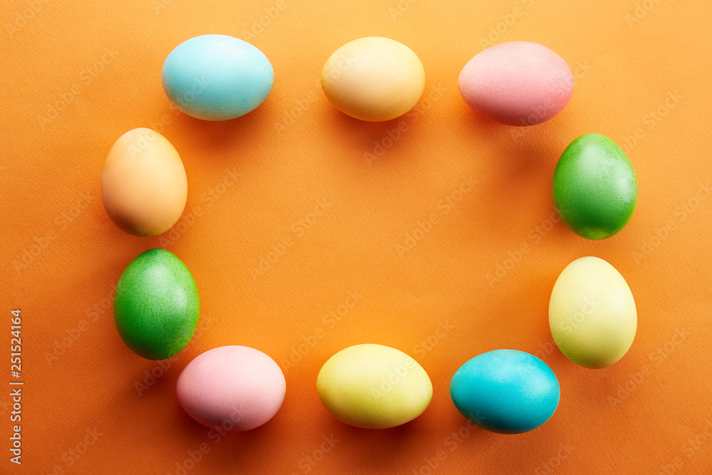 Bunch of blank painted Easter eggs of different pastel color on bright orange paper background with a lot of copy space for text. Top view, flat lay, close up. Easter greeting card concept.