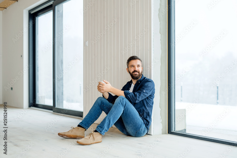 A mature man with cup of coffee sitting on the floor, furnishing new house. A mature man with cup of coffee sitting on the floor, furnishing new house.
