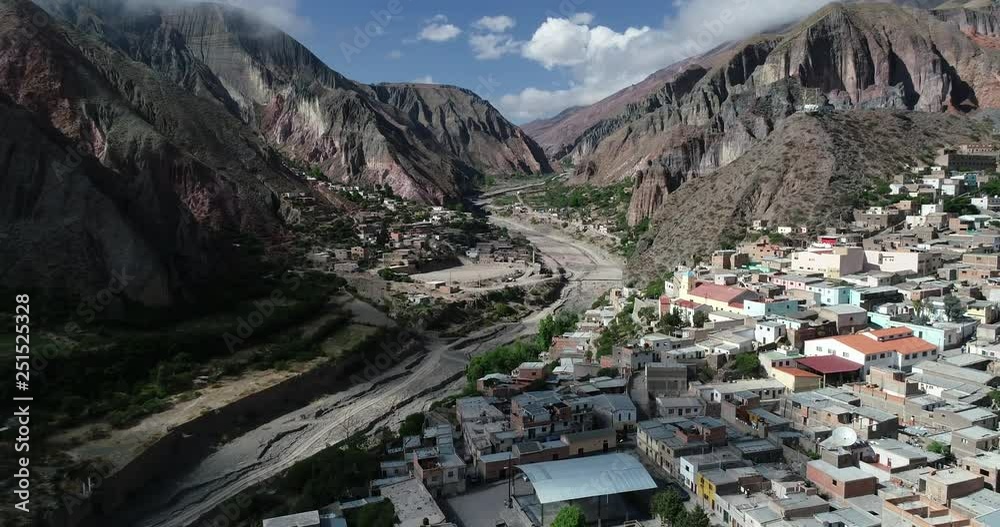 Aerial flying over Iruya, hidden town, at steep narrow valley surrounded of woods and dry colorful hills at background. Touristic town at Salta, Argentina