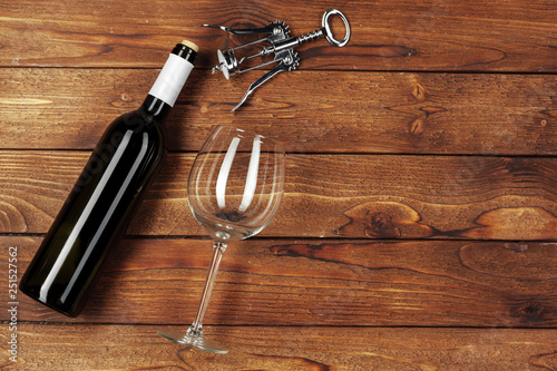 Red wine bottle, wine glass and corkscrew on wooden table background