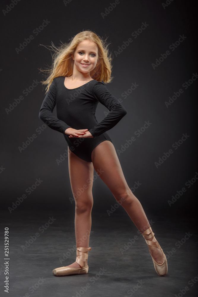 Cute little ballerina with long hair in a black leotard and pointe posing on a black background Cute little ballerina with long hair in a black leotard and pointe posing on a black background