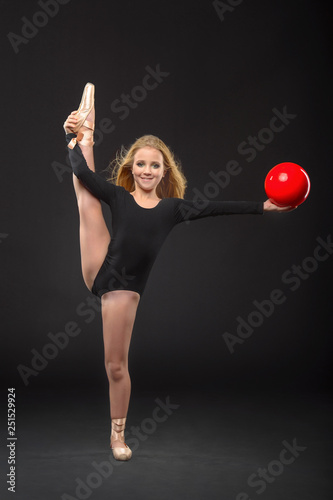 Cute little ballerina with long hair in a black leotard and pointe posing on a black background photo