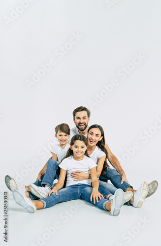 Relationship concept. Beautiful and happy smiling young family in white T-shirts are hugging and have a fun time together while sitting on the floor and looking on camera.