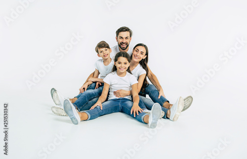 Relationship concept. Beautiful and happy smiling young family in white T-shirts are hugging and have a fun time together while sitting on the floor and looking on camera.