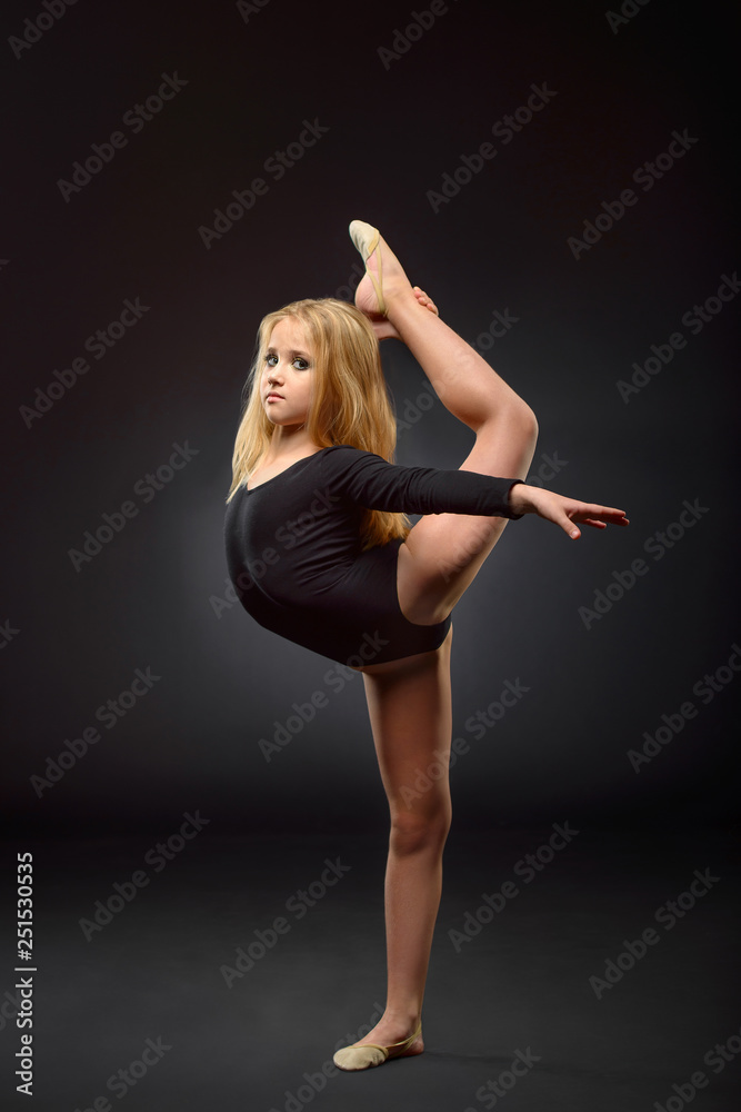 Young beautiful white caucasian girl gymnast with long hair doing gymnastic exercise on black background.