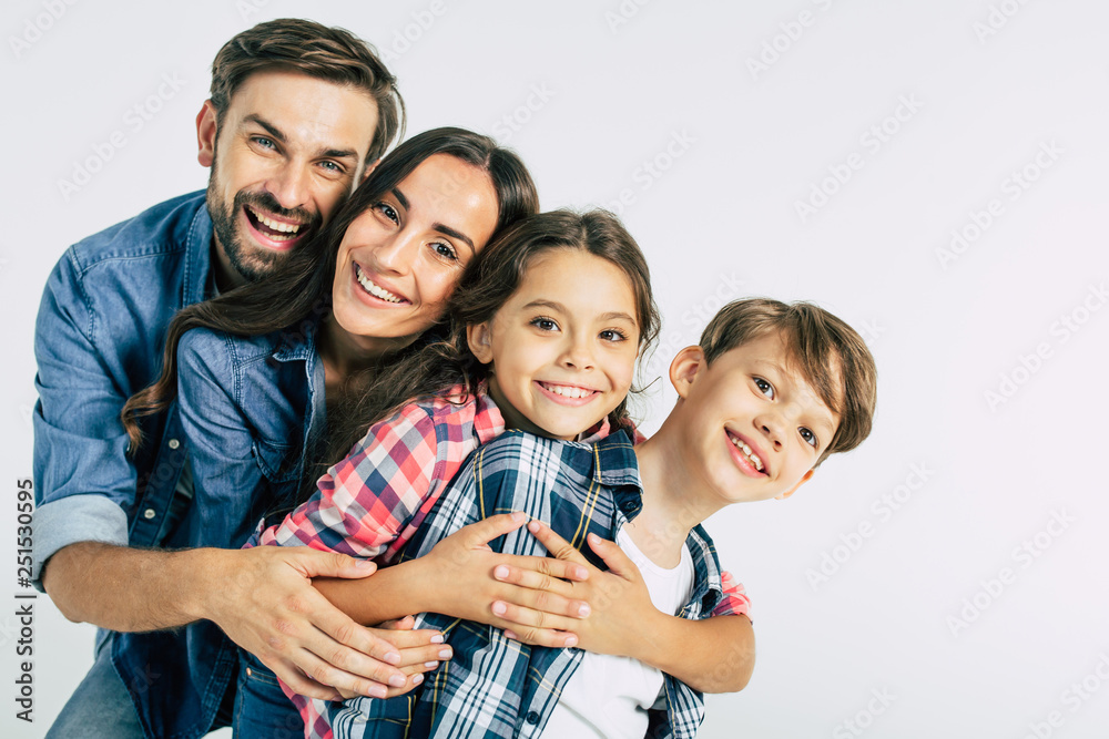 Power in big family. Dad and mommy hugging them beautiful kids and looking on the camera - obrazy, fototapety, plakaty 