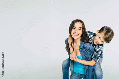 Quadro em tela Cute young smiling mother with son on her back isolated on white
