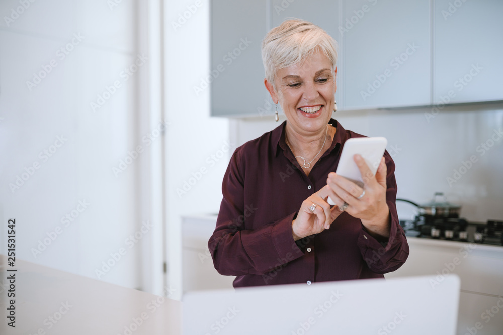 Portrait of a beautiful mature woman smiling, using her mobile phone, in the kitchen Portrait of a beautiful mature woman smiling, using her mobile phone, in the kitchen